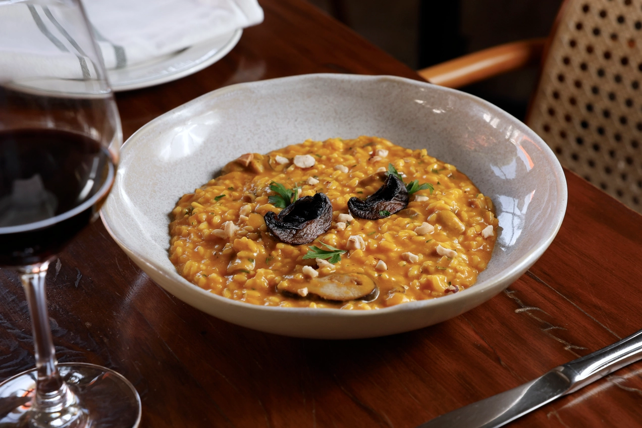 Yellow risotto with mushrooms, nuts, and a glass of wine on a restaurant table.