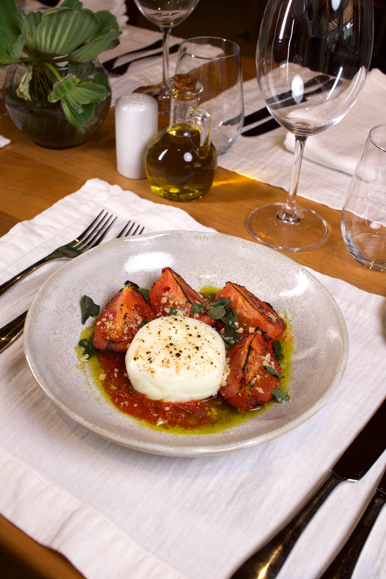 Burrata with grilled tomatoes, red sauce, and olive oil on a set table.