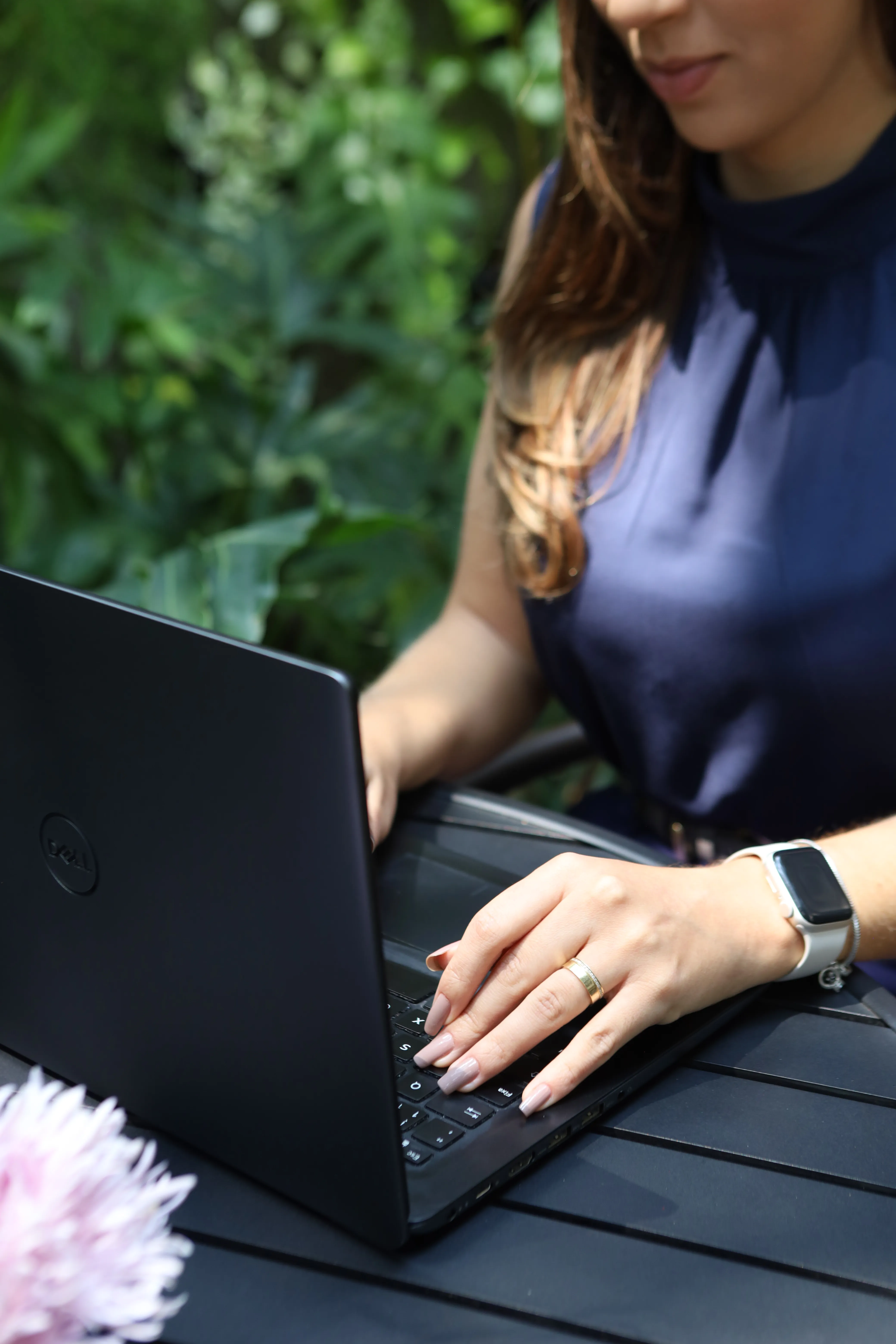 Una professionista lavora al laptop all’aperto, circondata da piante.