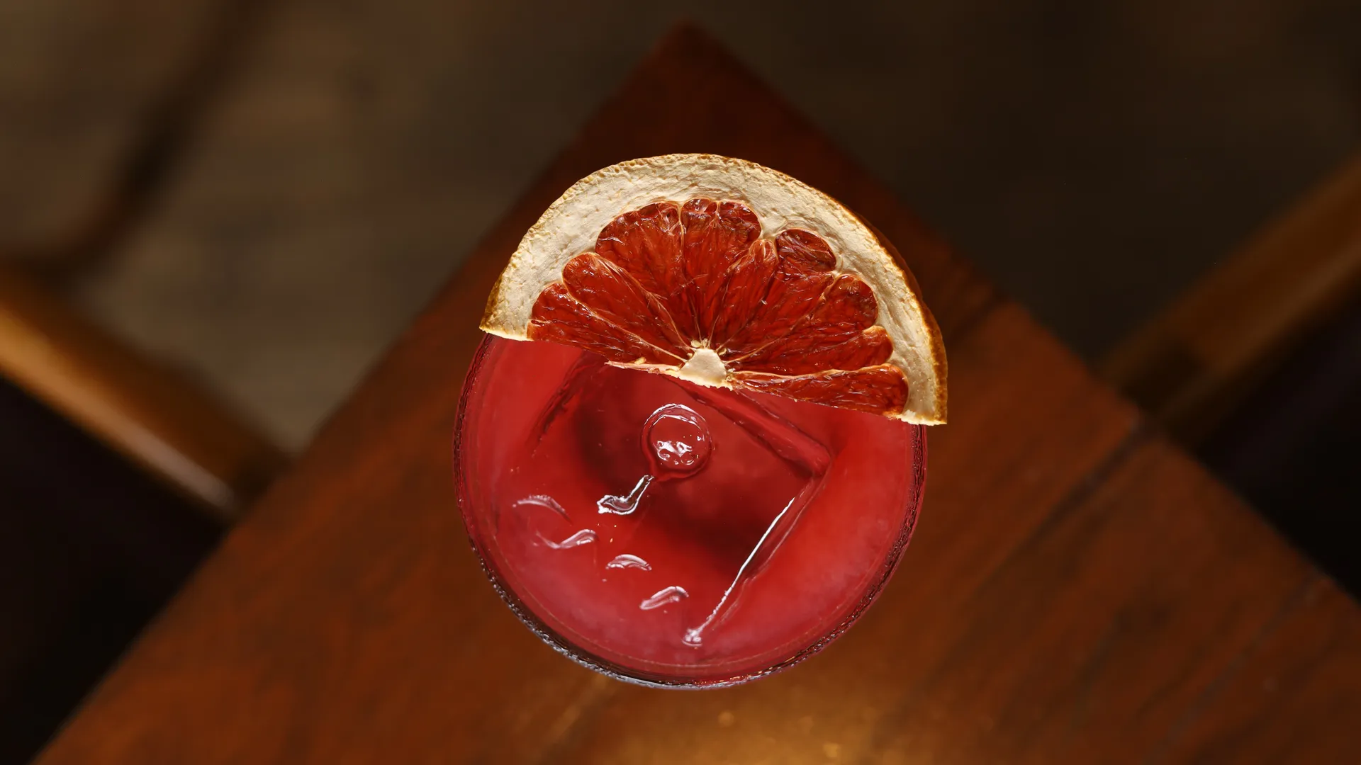 Red cocktail with a dried orange slice on a wooden table.