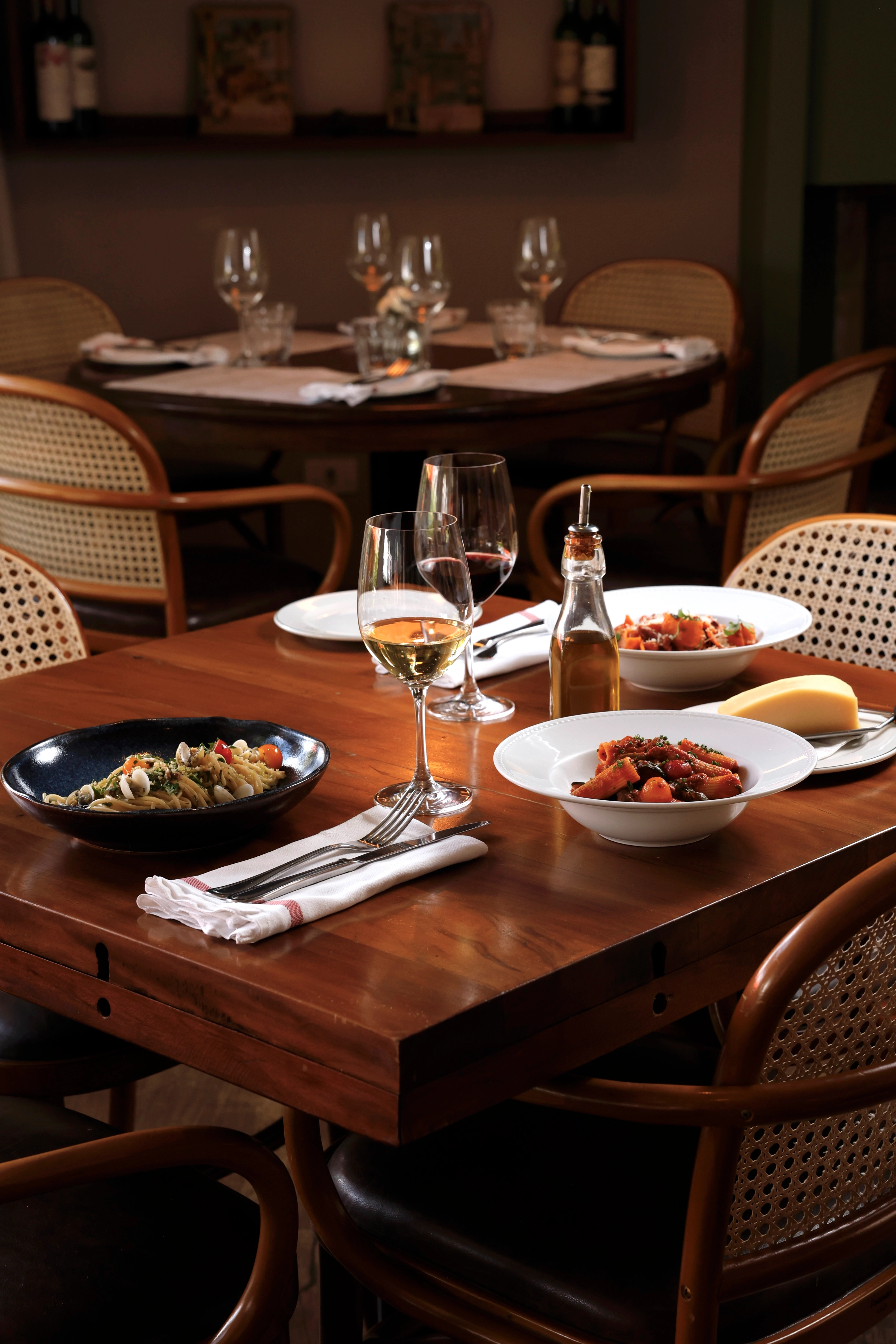 Tavolo da ristorante con piatti di pasta, vino e coperti pronti per gli ospiti.