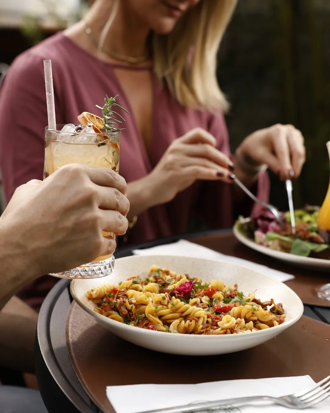 Un tavolo da ristorante con pasta, un drink e persone che condividono un pasto.